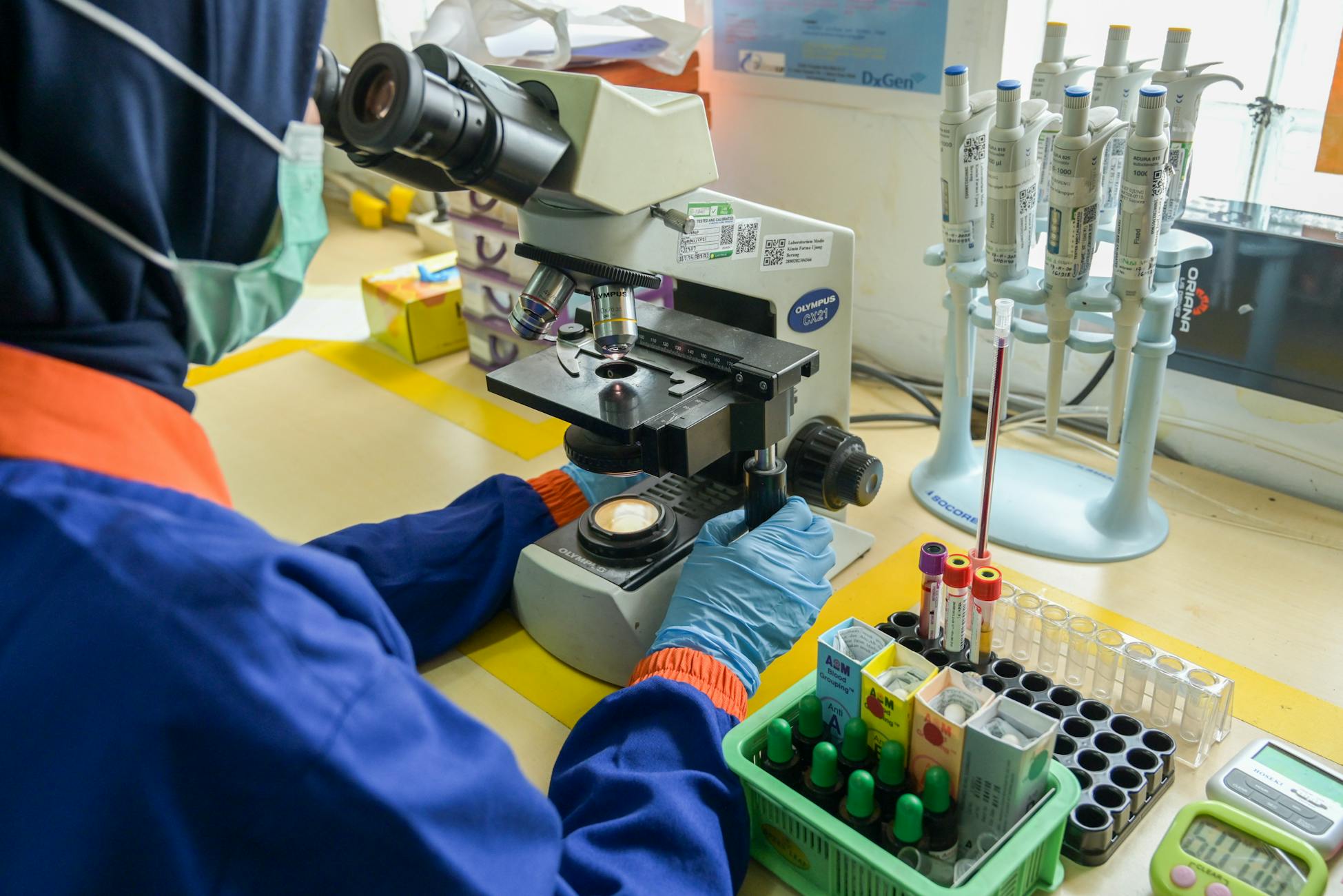 Technician in lab coat examining samples using a microscope in a modern laboratory setting.