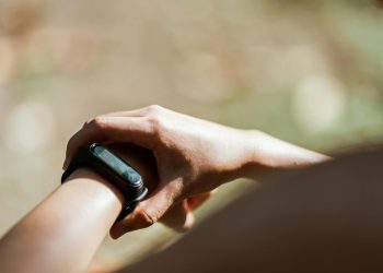 From above of crop anonymous person wearing modern bracelet with small display while standing outdoors on blurred background in daylight