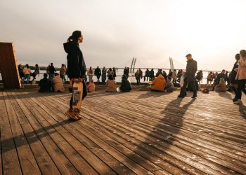 A group of people enjoying a sunny day on a wooden dock with a bridge in the background.