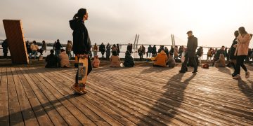 A group of people enjoying a sunny day on a wooden dock with a bridge in the background.