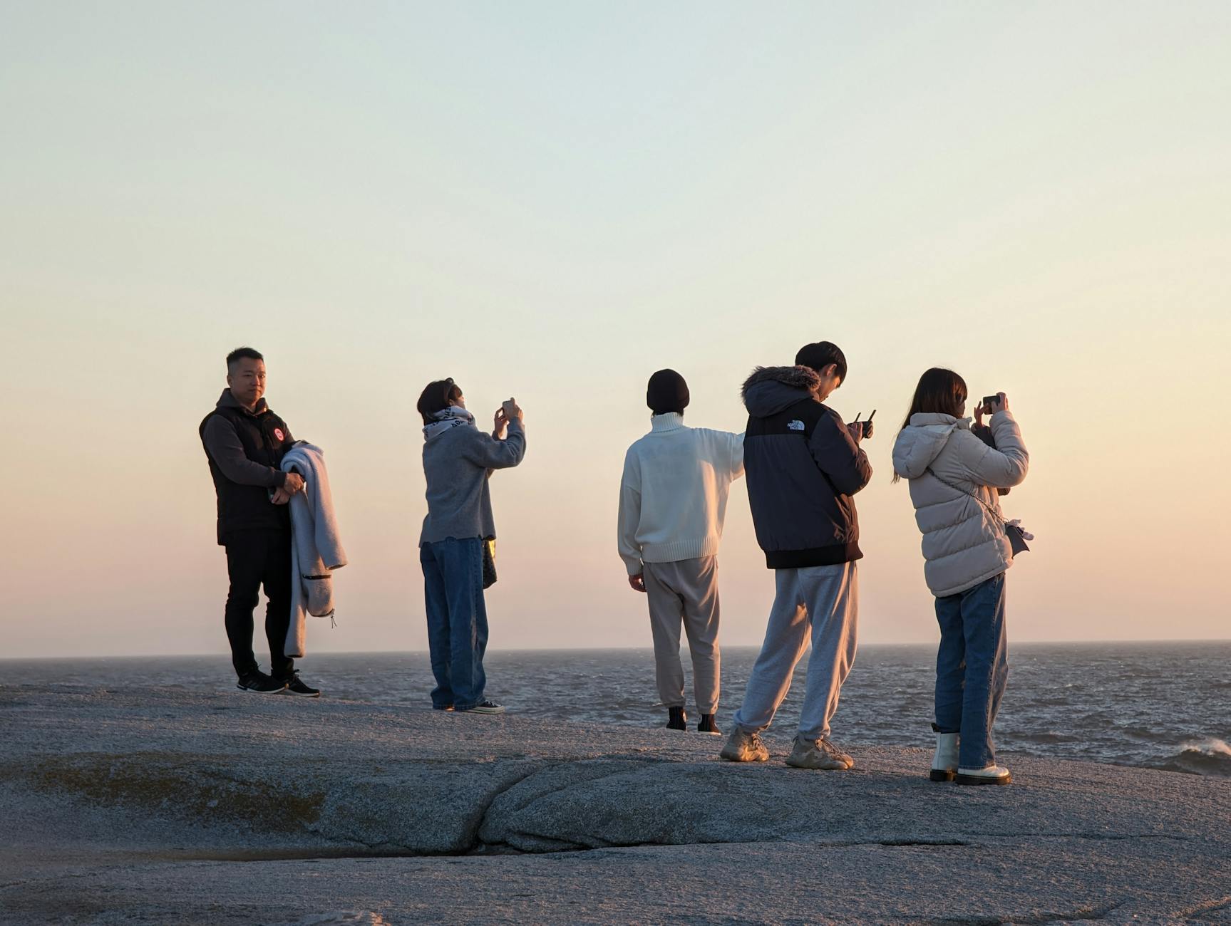 Group of people capturing sunset at Peggy's Cove, a scenic landmark in Nova Scotia.