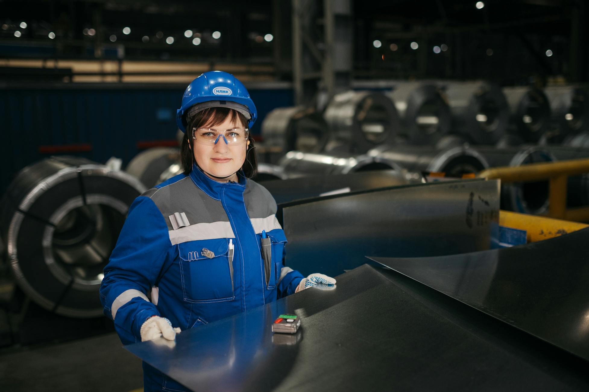 A woman in safety gear inspects metal sheets in a modern Russian industrial setting.