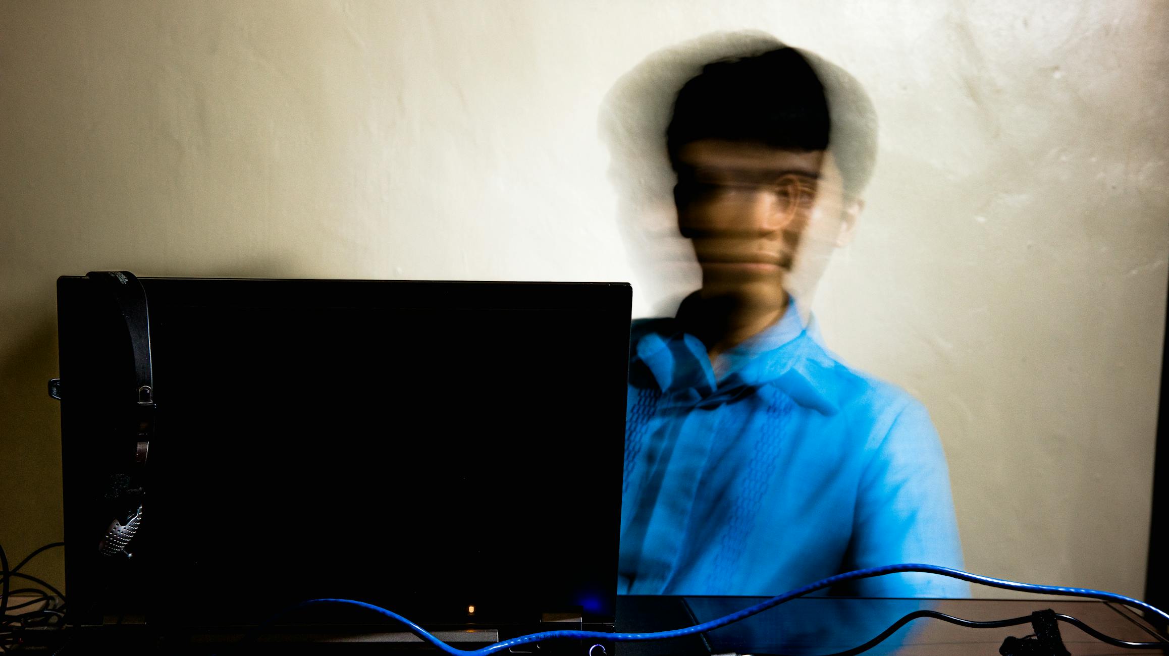 Long exposure of young concentrated male in casual wear sitting at table with netbook while working