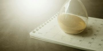 An hourglass on a calendar captures the essence of time management and urgency.