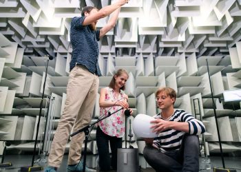 Engineers working together in a soundproof room to conduct acoustic testing with modern equipment.