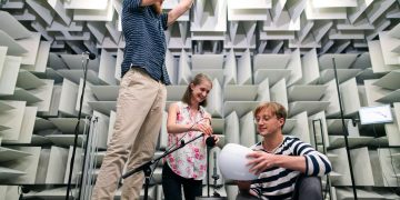 Engineers working together in a soundproof room to conduct acoustic testing with modern equipment.