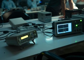 A dimly lit electronics lab featuring oscilloscopes and equipment on desks, creating a technical atmosphere.