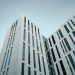 From below of contemporary multistory building with futuristic design and windows with unusual shapes located against cloudless blue sky on street of city