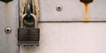 Close-up of a rusty metal padlock on a weathered door, highlighting security and decay.
