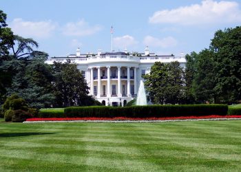 Iconic view of the White House with lush gardens and a central fountain on a sunny day.