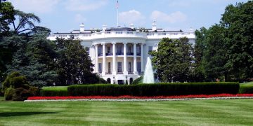 Iconic view of the White House with lush gardens and a central fountain on a sunny day.