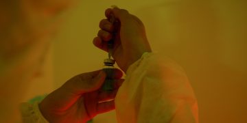 Close-up of a scientist handling a syringe and vial, highlighting laboratory work.