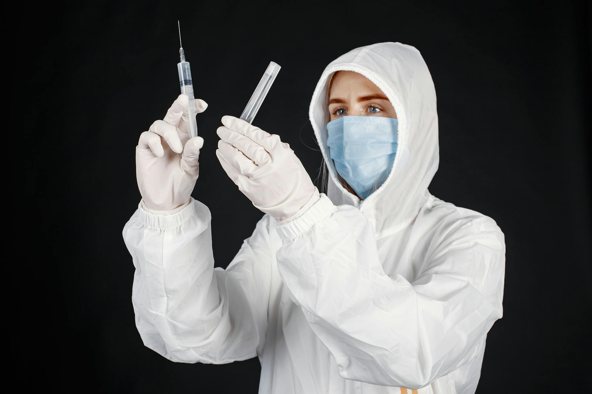 A scientist in protective gear prepares a syringe and vial for research purposes.