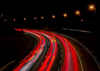 A captivating long exposure of a highway at night, showcasing vibrant light trails under streetlamps.