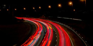 A captivating long exposure of a highway at night, showcasing vibrant light trails under streetlamps.