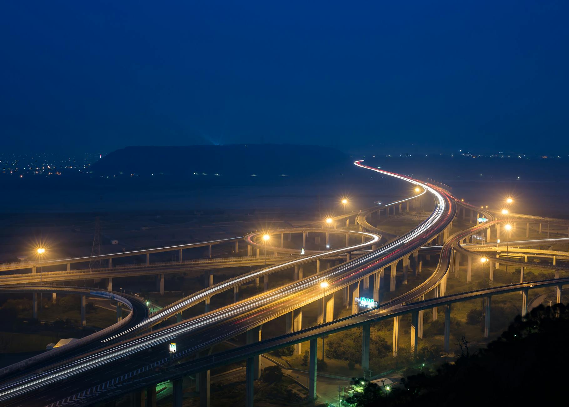 From above of glowing lamps on contemporary city road junction above greenery and broad river at night