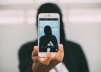 A person in a hoodie takes a mysterious selfie with a smartphone.