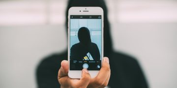 A person in a hoodie takes a mysterious selfie with a smartphone.