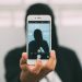 A person in a hoodie takes a mysterious selfie with a smartphone.