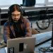 Bearded male developer in headphones coding on a laptop in a modern office setting.