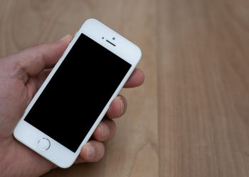 A person holding a smartphone with a blank screen over a wooden surface. Great for mockup use.