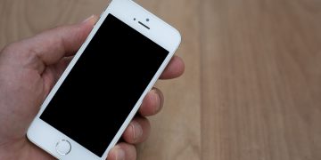 A person holding a smartphone with a blank screen over a wooden surface. Great for mockup use.