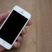A person holding a smartphone with a blank screen over a wooden surface. Great for mockup use.