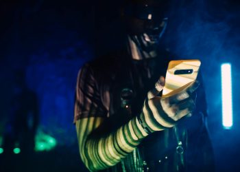 A person with futuristic makeup using a smartphone in a cyberpunk setting.