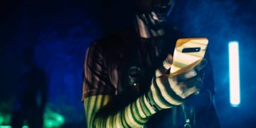 A person with futuristic makeup using a smartphone in a cyberpunk setting.