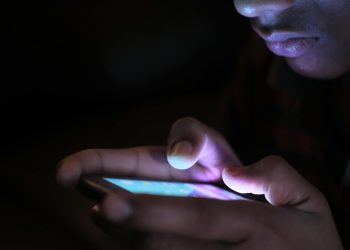 Close-up of a person holding and using an illuminated smartphone in a dark setting.