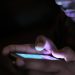 Close-up of a person holding and using an illuminated smartphone in a dark setting.