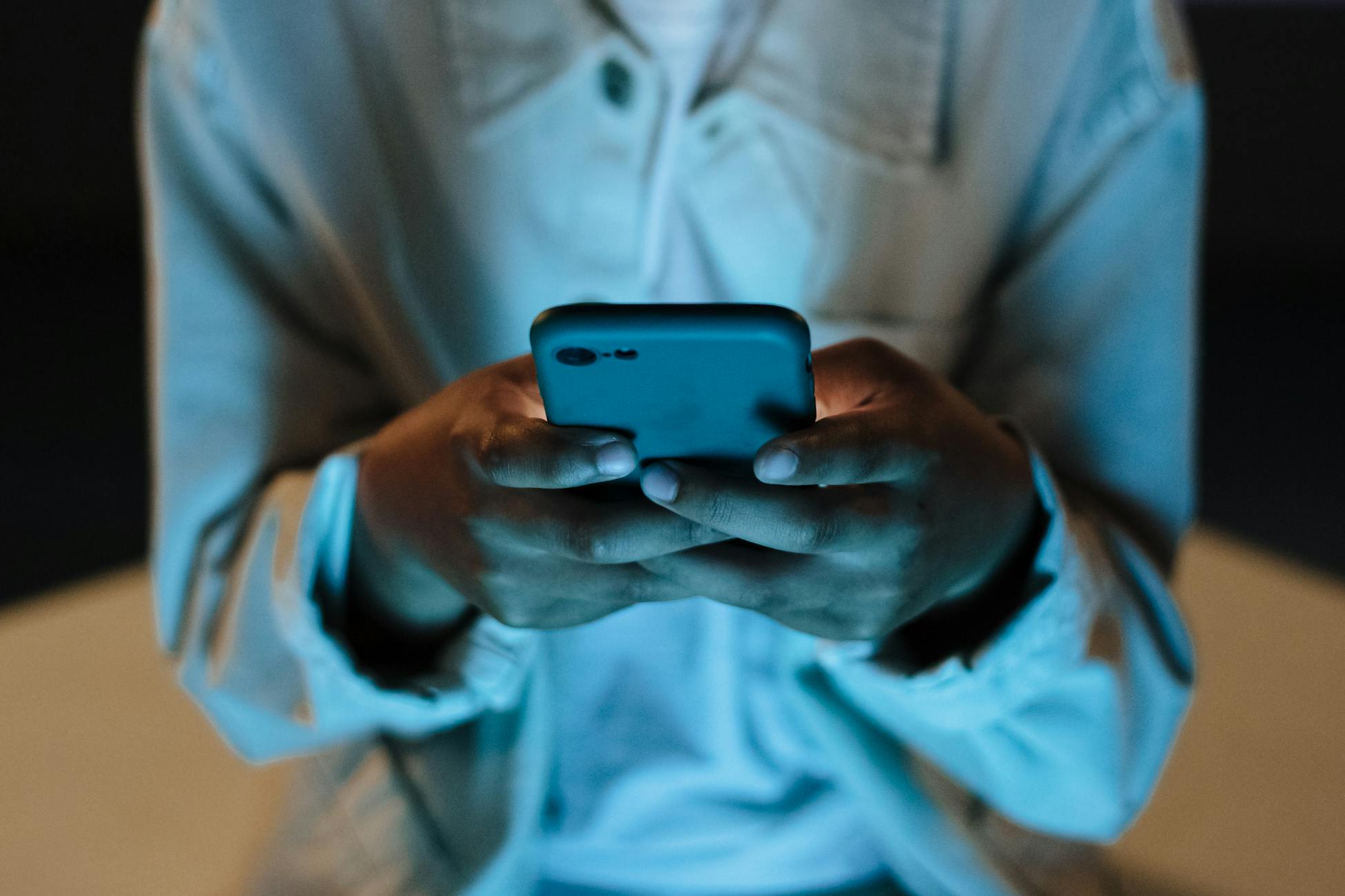 Adult using a smartphone indoors at night, highlighting technology use.