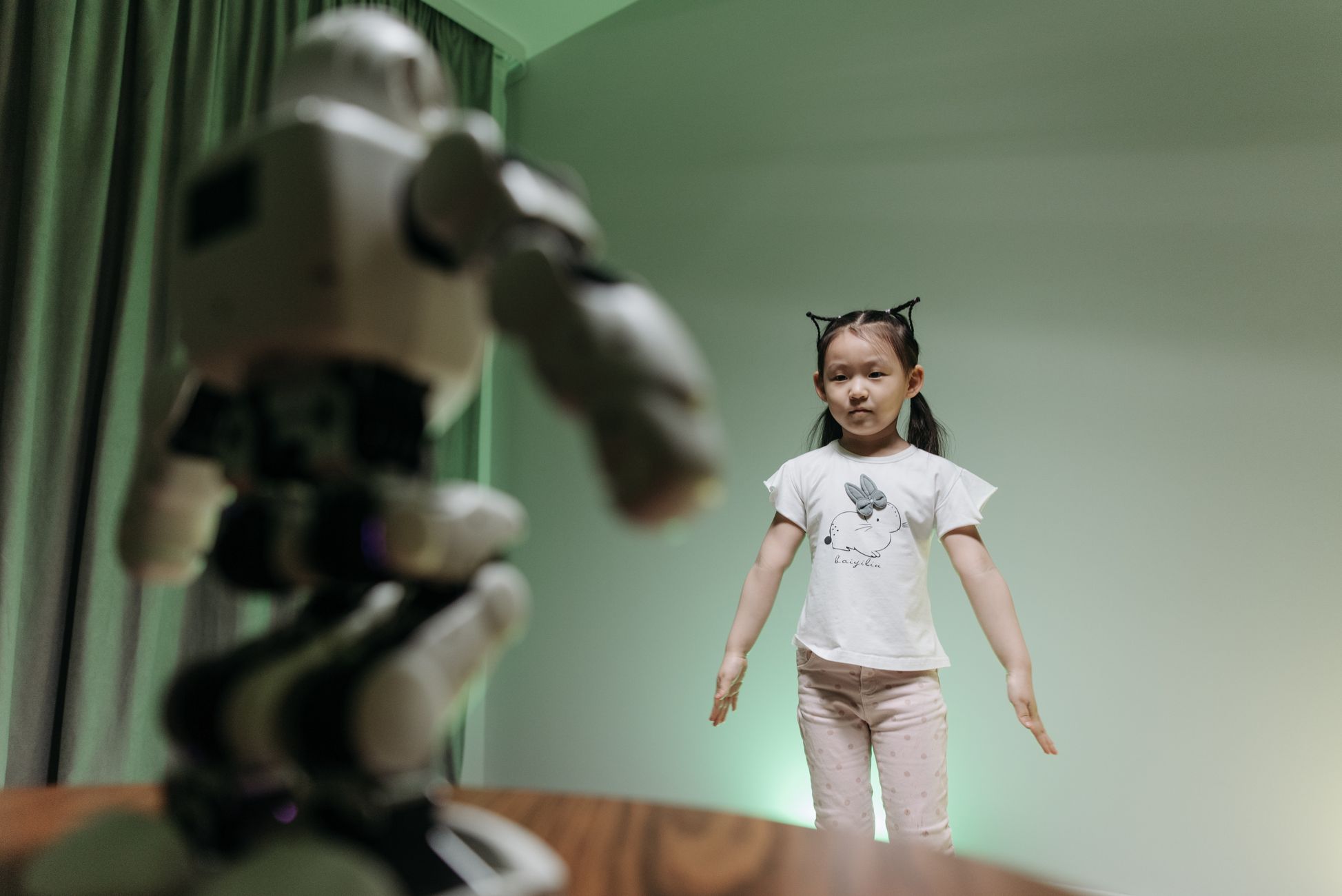 An Asian child interacts with a humanoid robot indoors, embracing innovation and play.