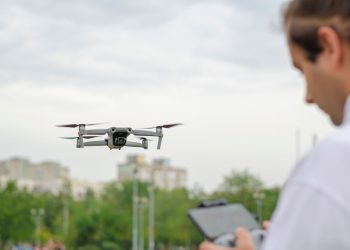 Drone in flight piloted by a person in a city park, capturing urban landscape.