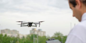 Drone in flight piloted by a person in a city park, capturing urban landscape.