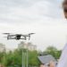 Drone in flight piloted by a person in a city park, capturing urban landscape.
