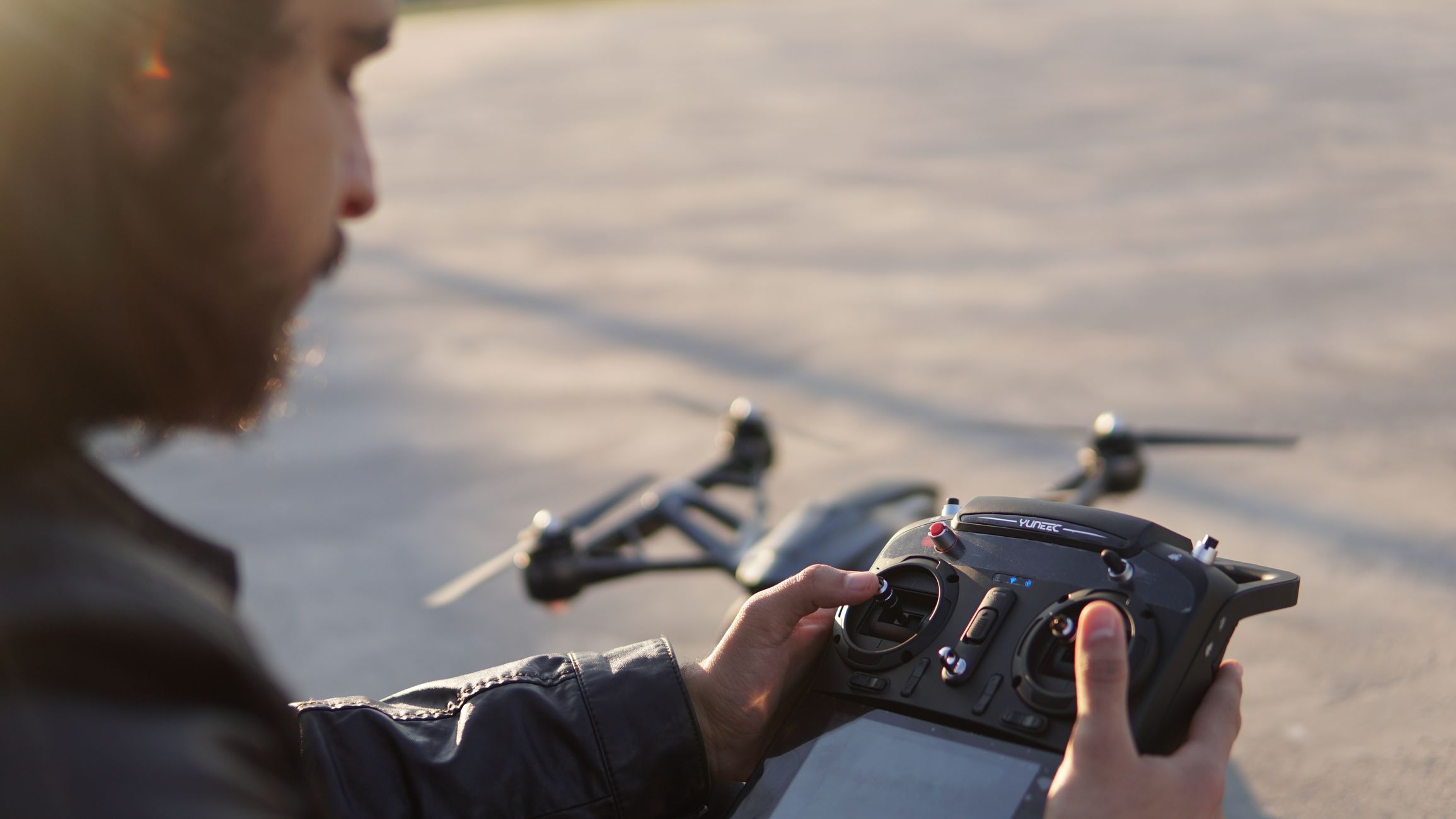 From above of crop bearded male operator controlling drone with remote control with display at daytime