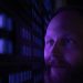 Close-up of a bearded man looking contemplatively at a purple-lit wall.