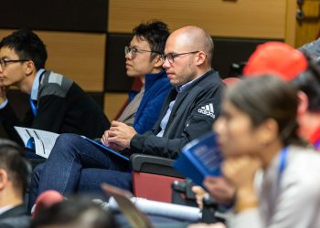 A diverse group of adults attentively listening to a lecture in an indoor conference setting.