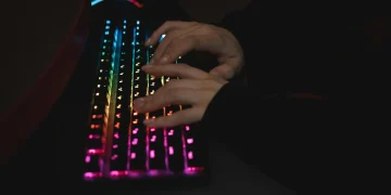 Close-up of hands typing on a colorful RGB backlit mechanical keyboard in a dimly lit environment.
