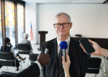 Senior man in formal attire being interviewed in a conference room.