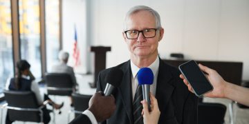 Senior man in formal attire being interviewed in a conference room.