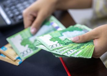 Person counting stacks of Uzbekistani som banknotes, showcasing financial transactions.
