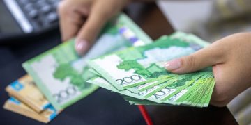 Person counting stacks of Uzbekistani som banknotes, showcasing financial transactions.