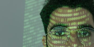 Close-up of a man with binary code projected on his face, symbolizing cybersecurity.