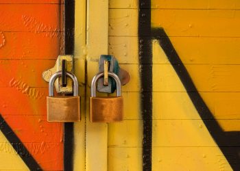 Close-up of two brass padlocks securing a vibrant graffiti-painted door, symbolizing security.