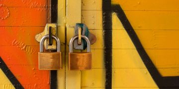 Close-up of two brass padlocks securing a vibrant graffiti-painted door, symbolizing security.
