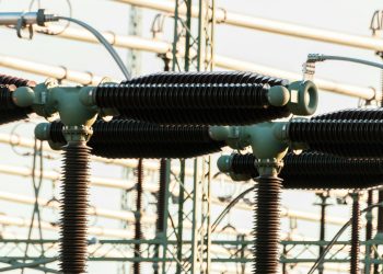 Close-up of outdoor electrical power equipment with insulators and conductors.