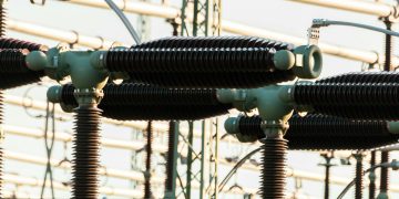 Close-up of outdoor electrical power equipment with insulators and conductors.
