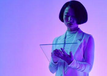 Woman interacts with a transparent digital screen in vibrant studio lighting.